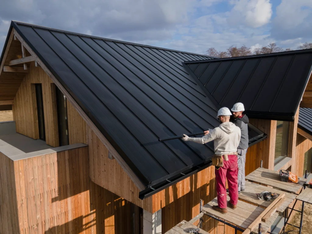 Professional roof installation on a modern residential property, showing two workers installing a new metal roof with safety helmets and construction equipment.